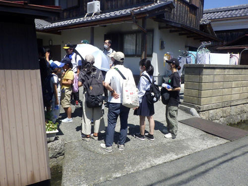 （民家の中での説明を聞く参加者）